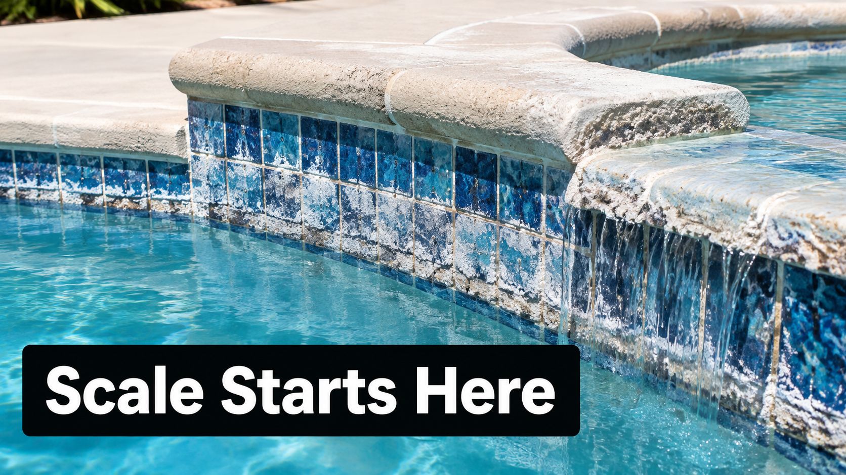 A close-up view of a swimming pool water feature showing significant white calcium scaling on blue tiles.